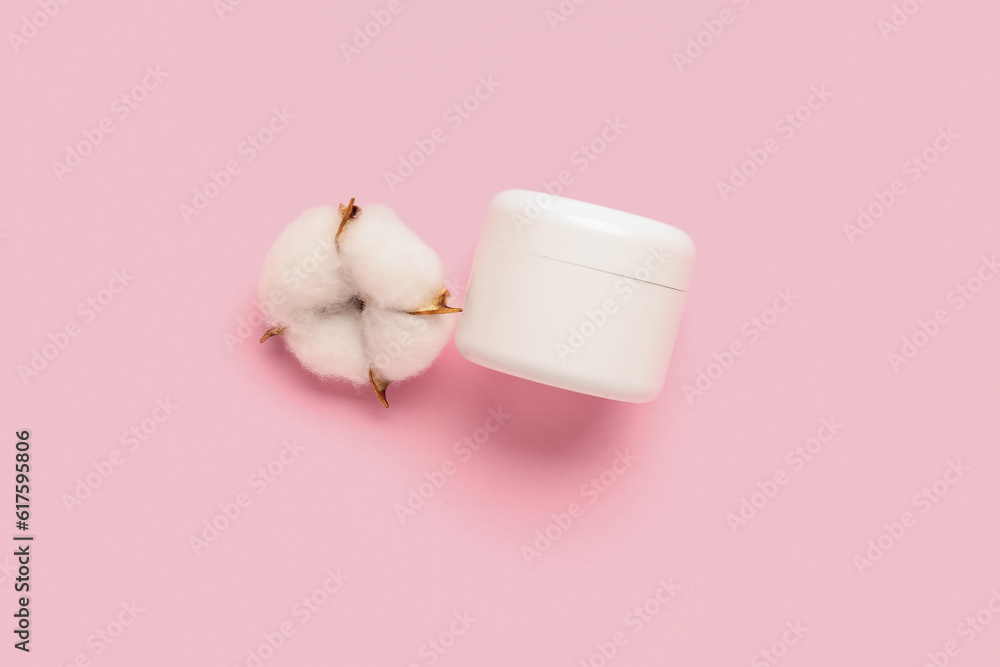 Jar of cosmetic product and cotton flower on pink background