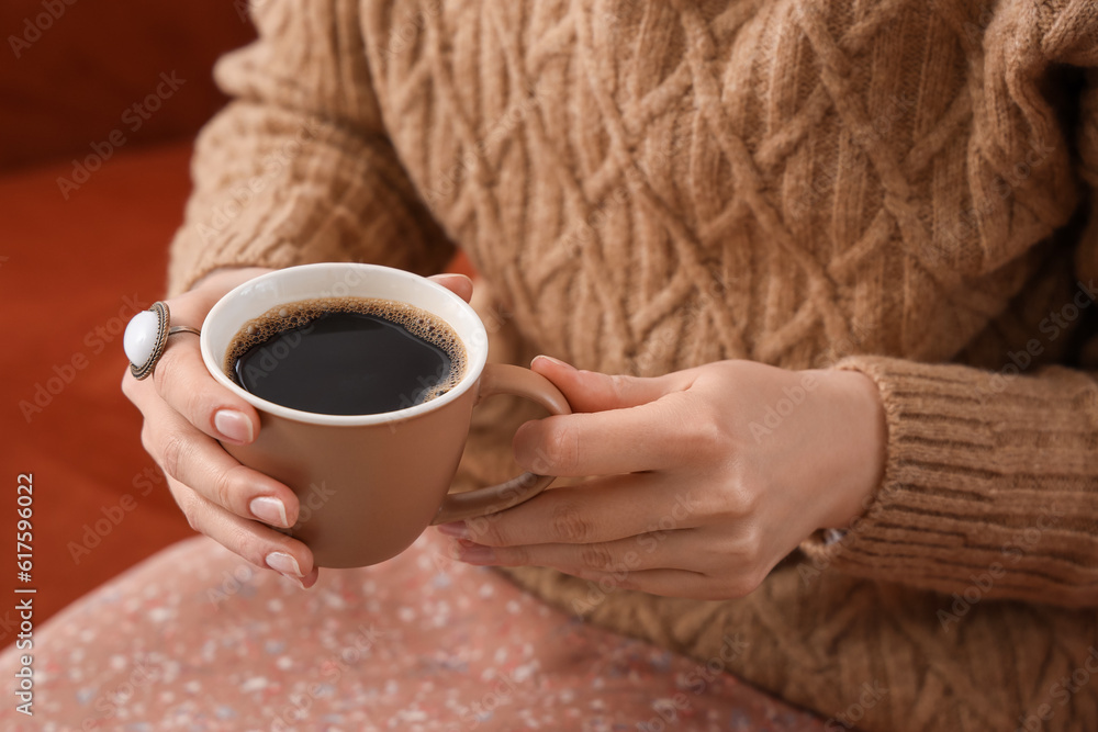 Woman sitting on cozy sofa and holding cup of delicious coffee