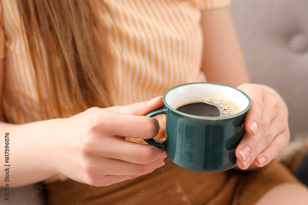 Woman sitting on cozy armchair and holding cup of delicious coffee