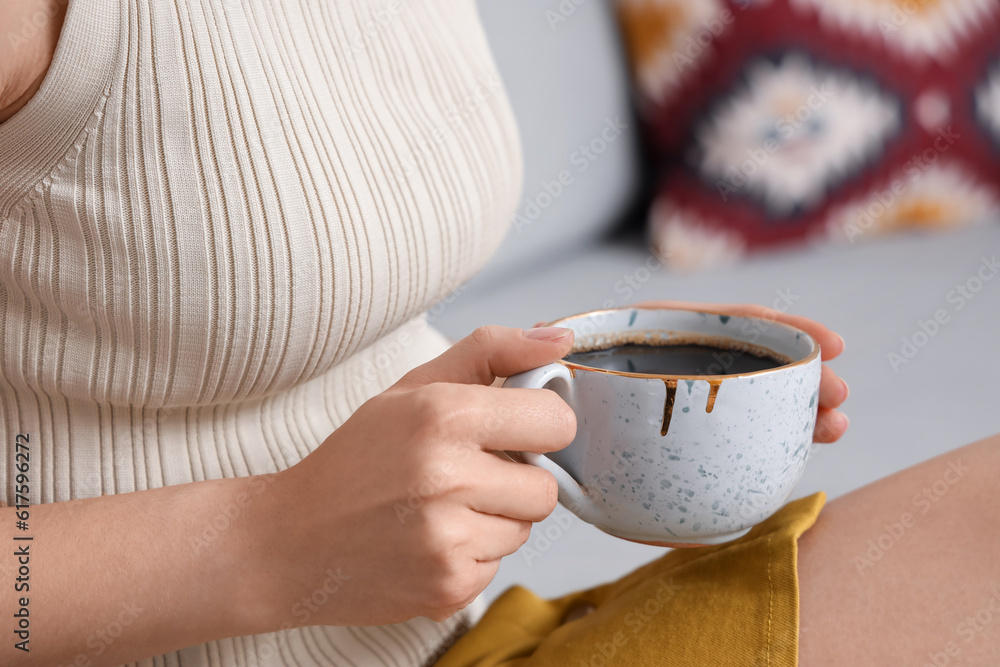 Woman sitting on cozy sofa and holding cup of delicious coffee