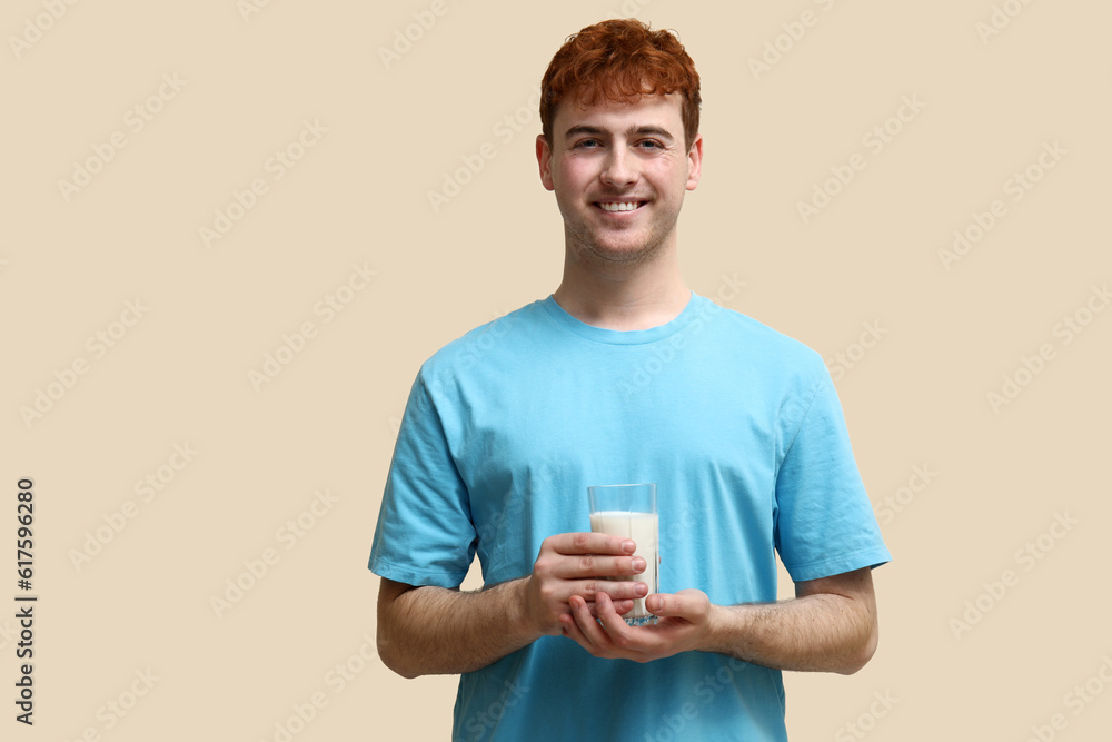 Young man with glass of milk on beige background