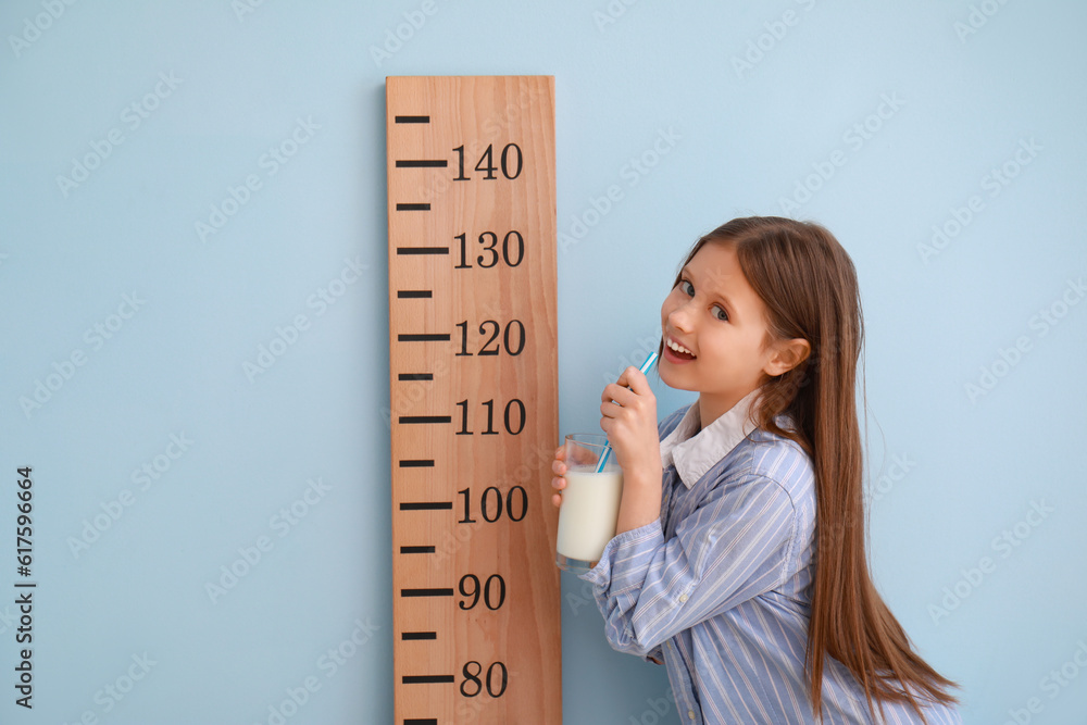 Little girl with glass of milk and stadiometer on light blue background