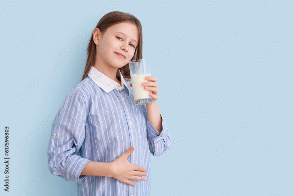 Little girl with glass of milk on light blue background