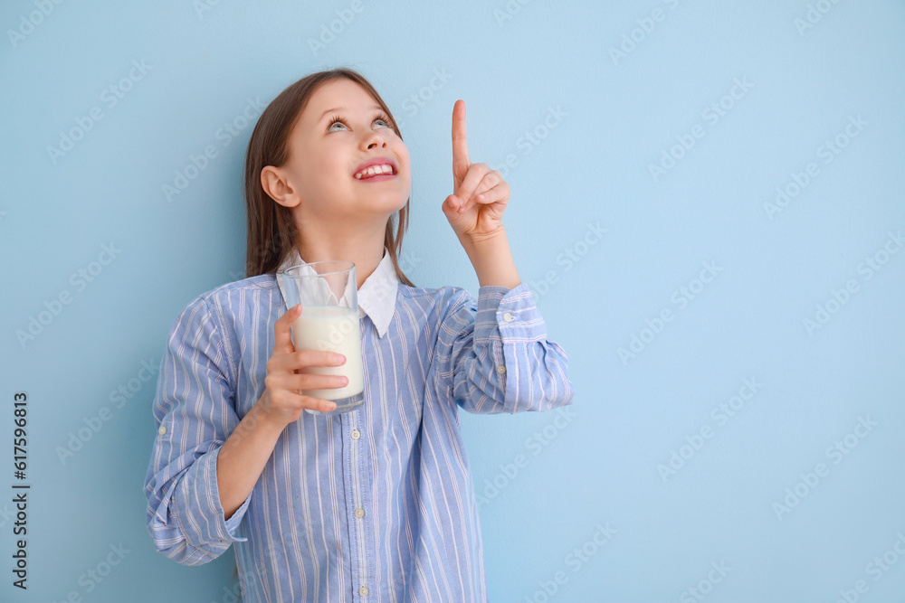 Little girl with glass of milk pointing at something on light blue background