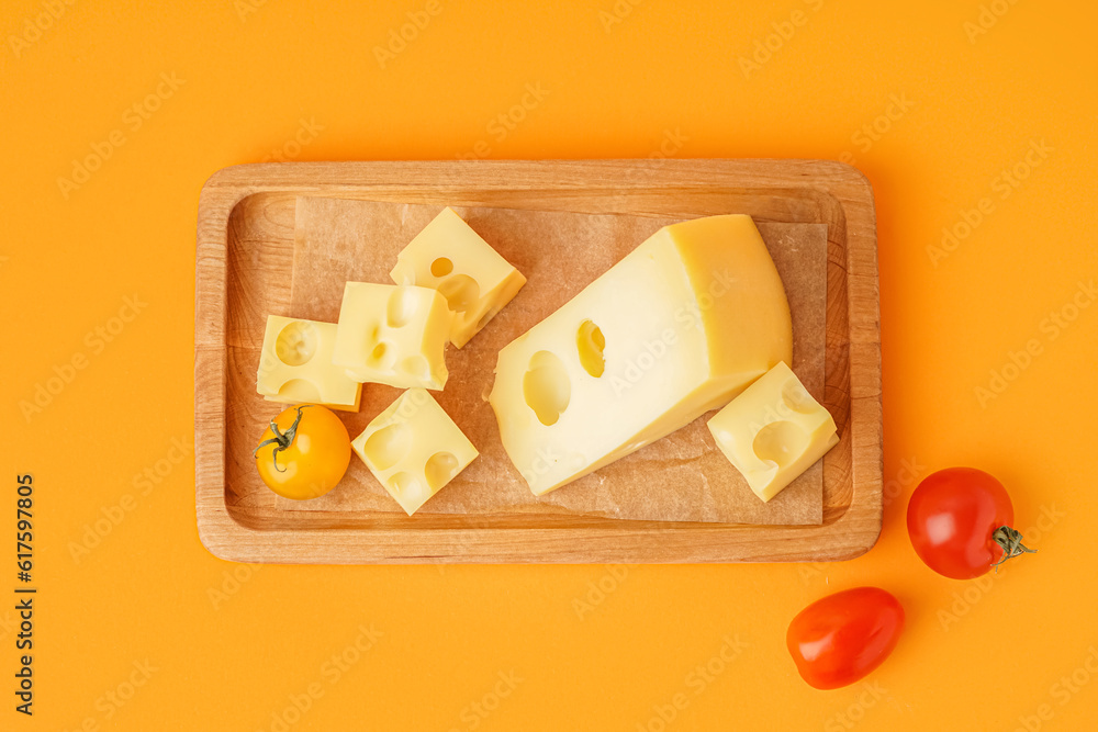 Board with pieces of Swiss cheese and tomatoes on orange background