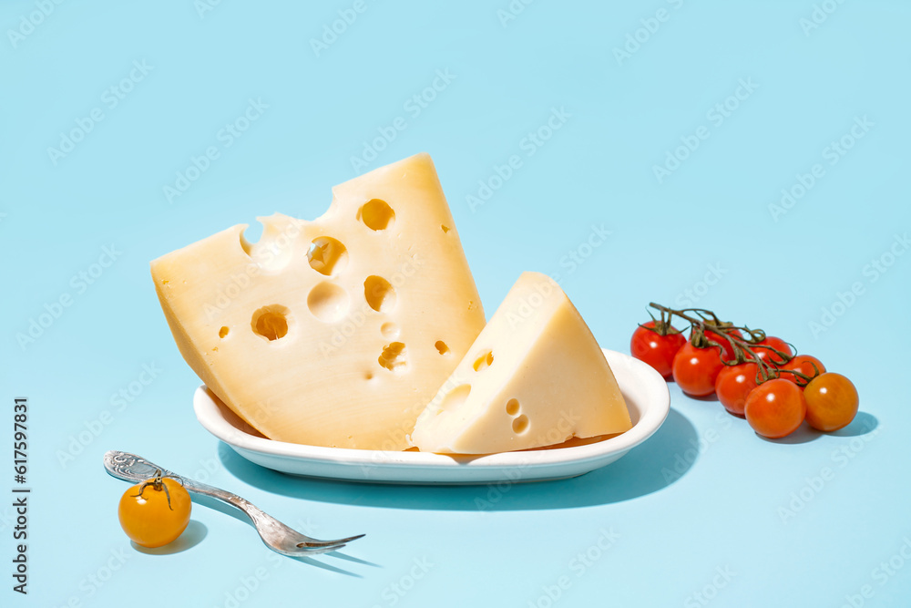 Plate with pieces of Swiss cheese and tomatoes on blue background