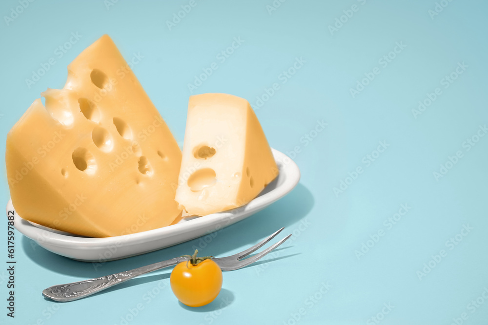 Plate with pieces of Swiss cheese and tomato on blue background