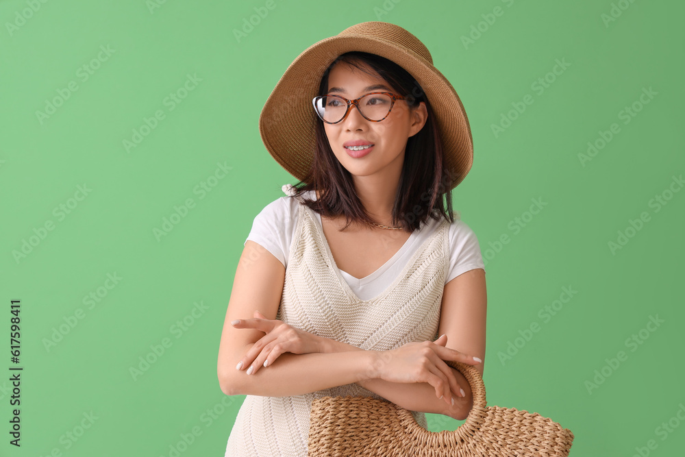 Beautiful Asian woman in stylish eyeglasses with bag on green background