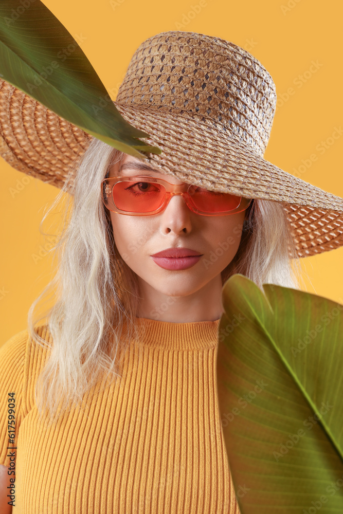 Young woman in stylish sunglasses with palm leaves on orange background, closeup