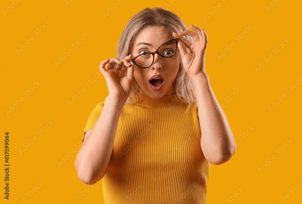 Surprised young woman in stylish eyeglasses on orange background