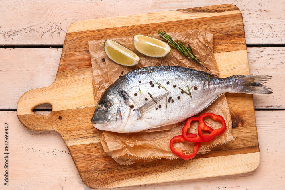 Board of raw dorado fish with lime and rosemary on light wooden background