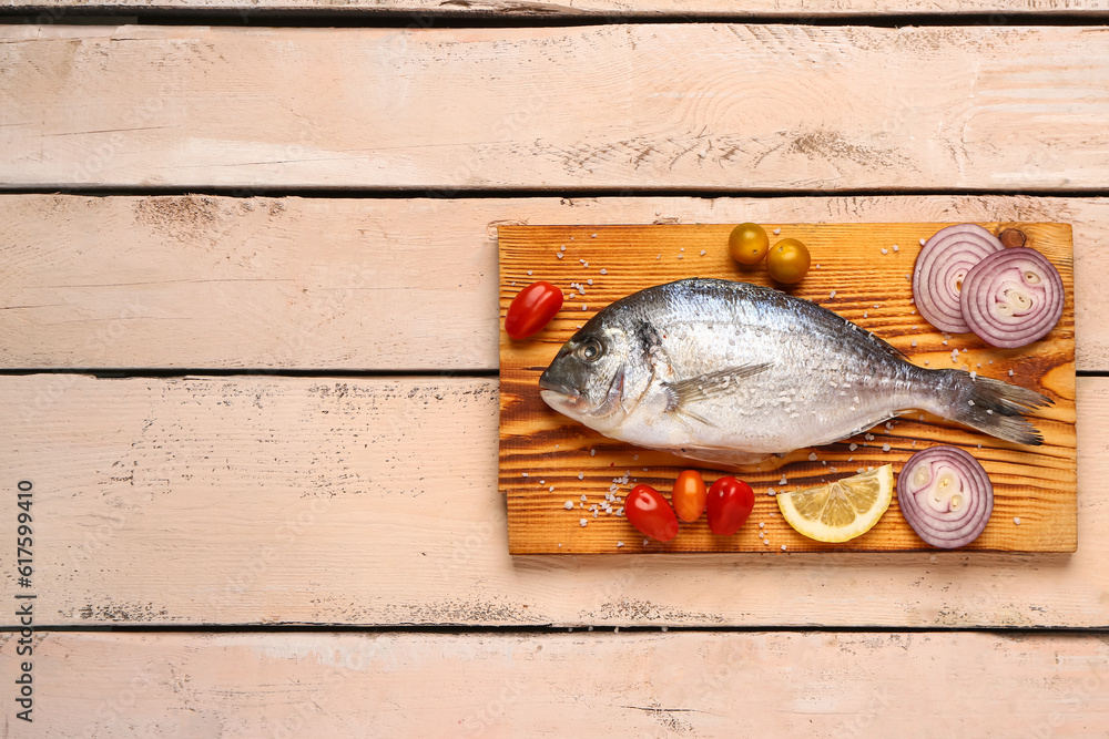 Board of raw dorado fish with lemon and vegetables on light wooden background