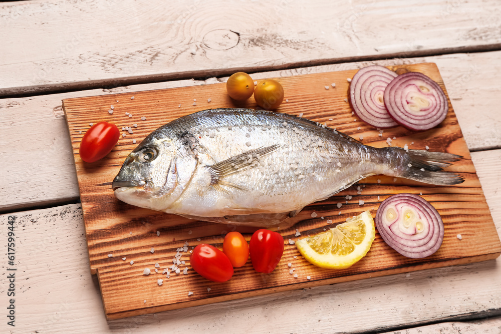 Board of raw dorado fish with lemon and vegetables on light wooden background