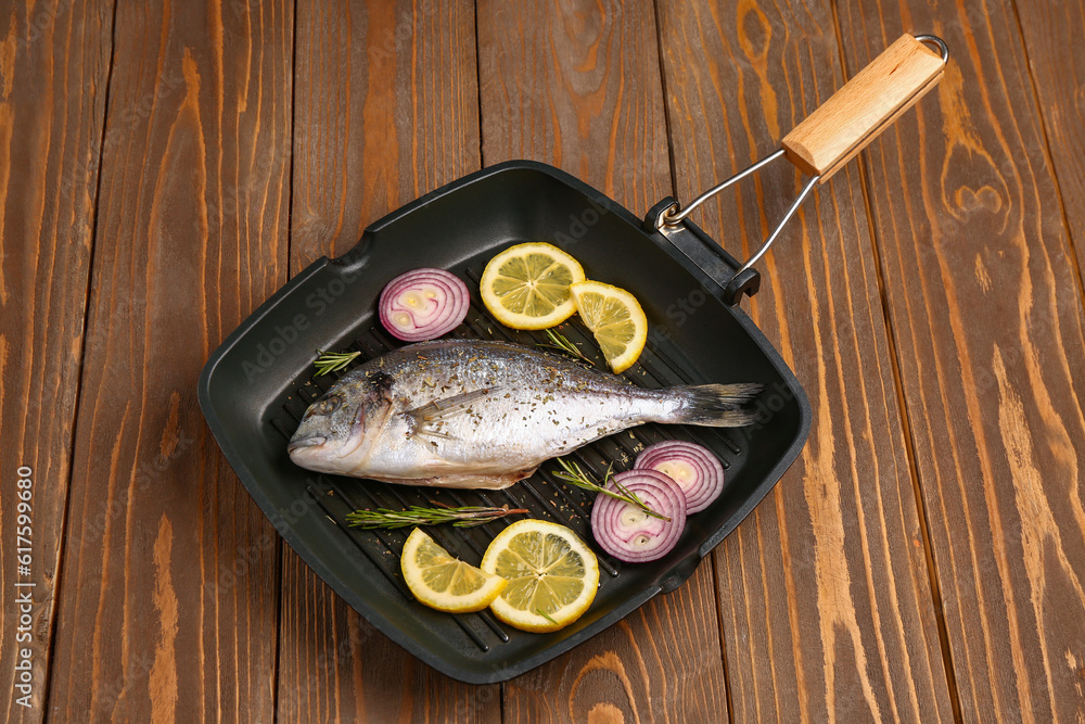 Grill pan of raw dorado fish with lemon and onion on wooden background