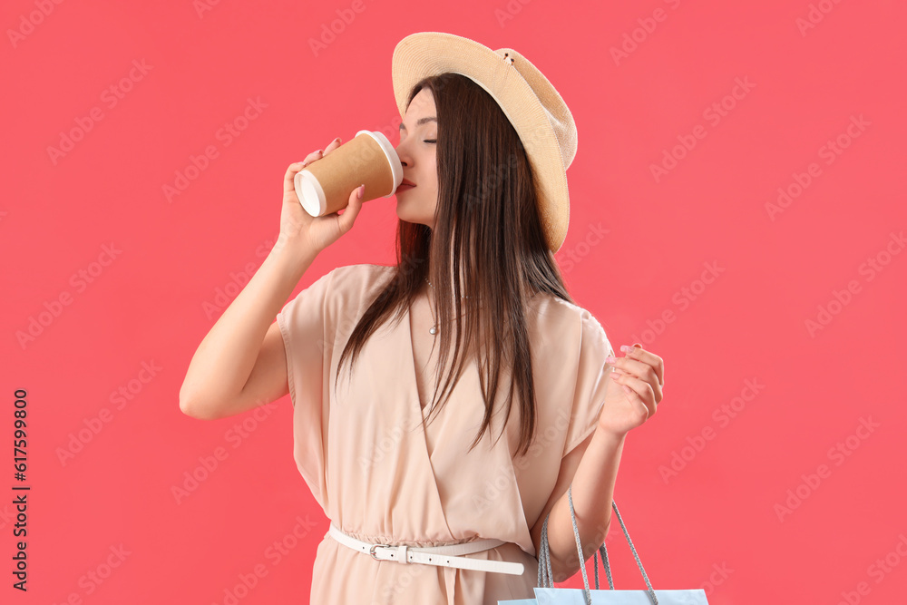 Young woman with shopping bags drinking coffee on red background