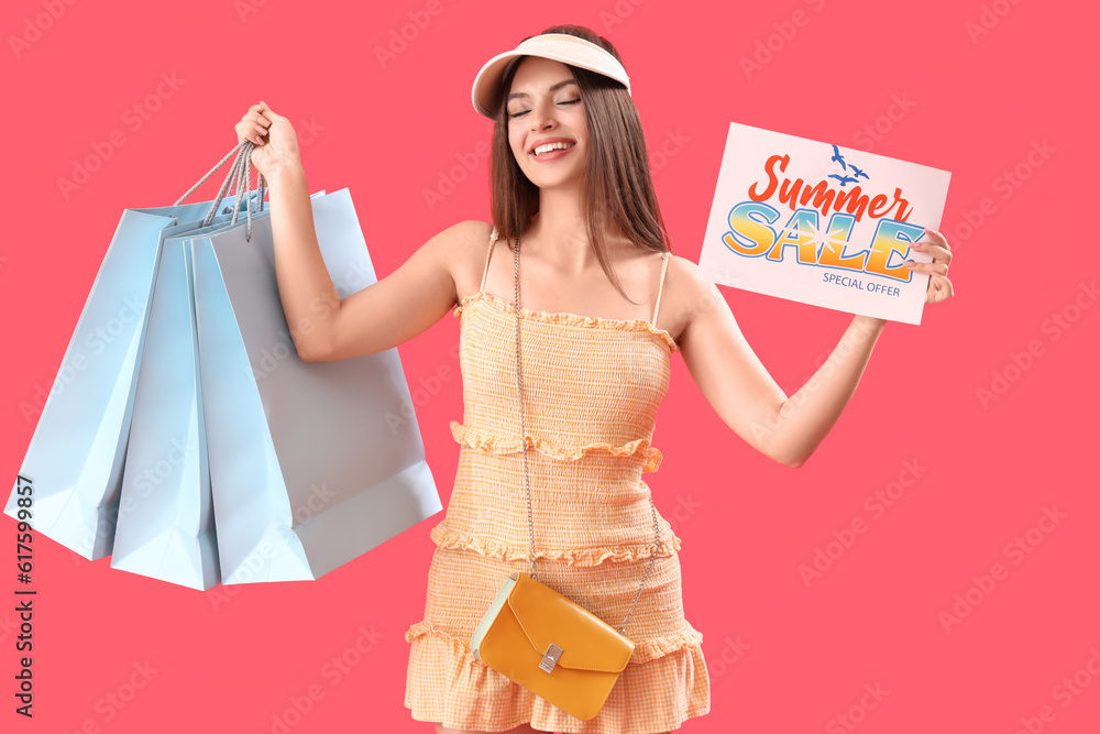 Young woman holding paper with text SUMMER SALE and shopping bags on red background