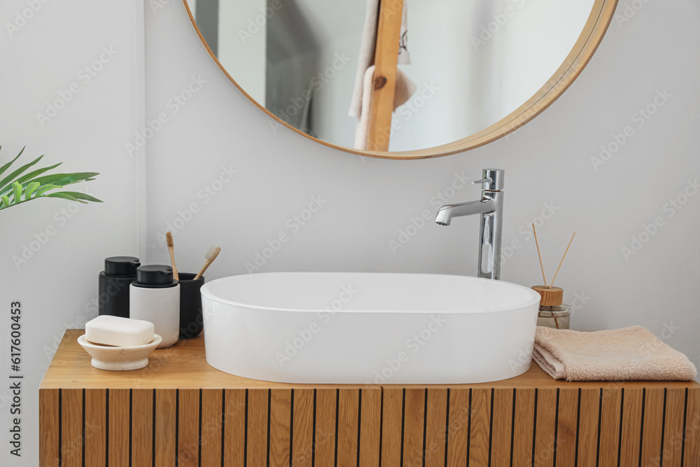 Sink bowl, soap bar, toothbrushes and bath accessories on wooden cabinet in bathroom