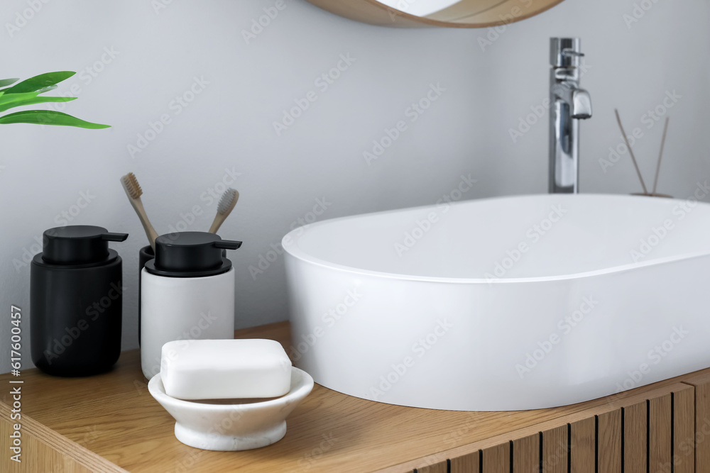 Sink bowl, soap bar, toothbrushes and bath accessories on wooden cabinet in bathroom