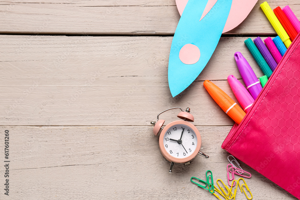 Blue paper rocket with alarm clock, markers and clips on beige wooden background