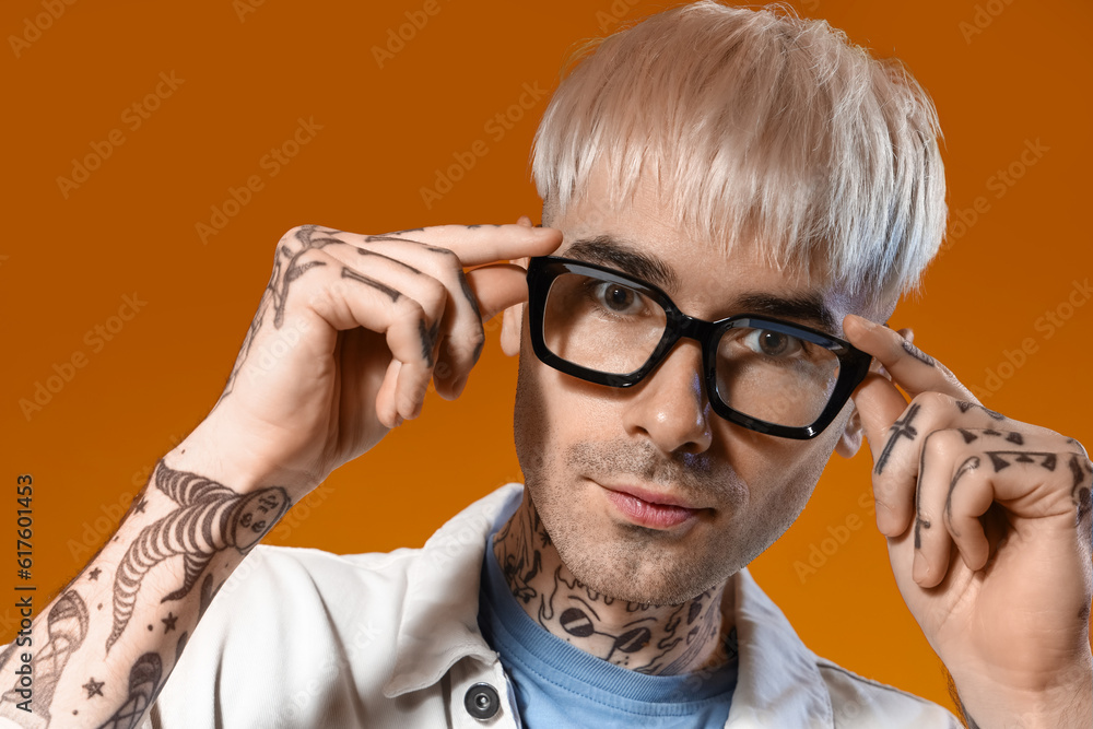 Young tattooed man in stylish eyeglasses on color background, closeup