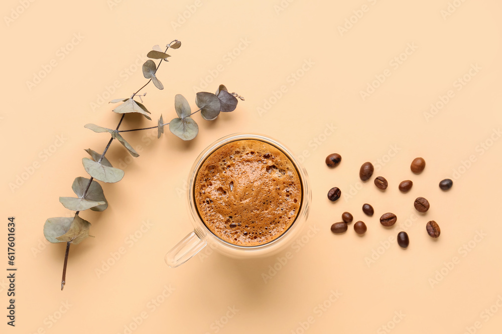 Glass cup of hot espresso and coffee beans with eucalyptus on beige background