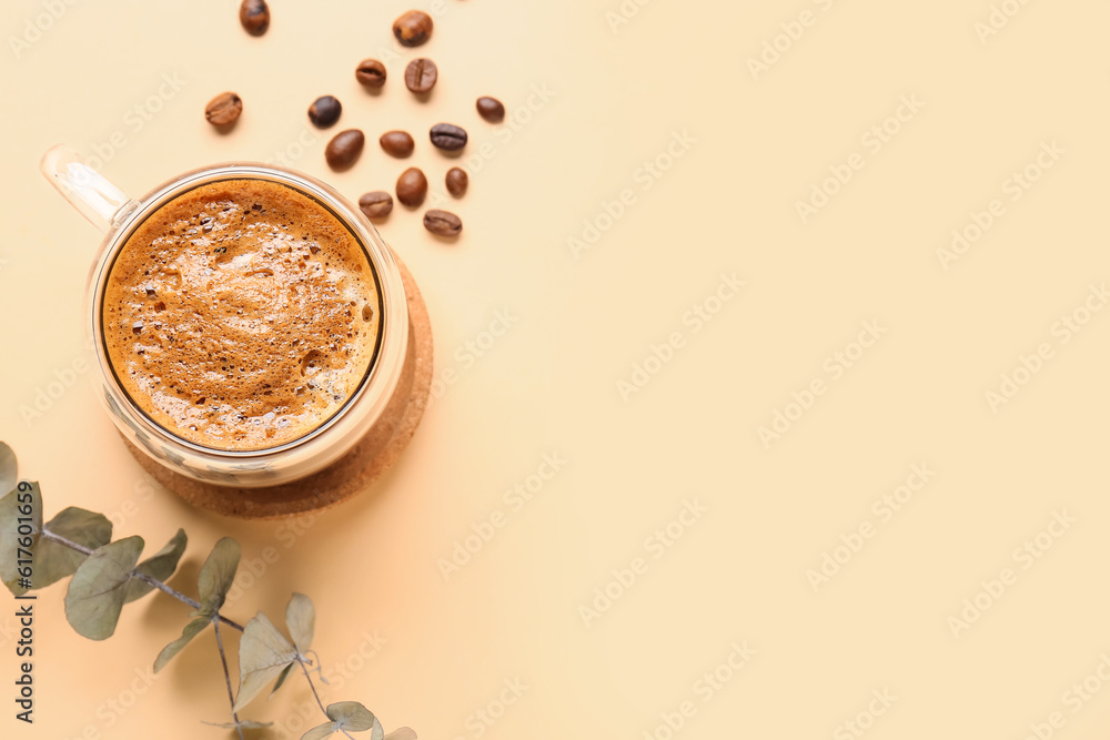 Glass cup of hot espresso and coffee beans with eucalyptus on beige background