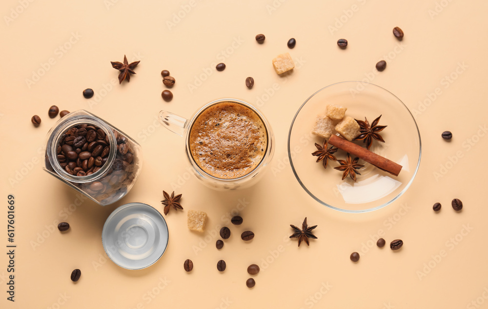 Glass cup of hot espresso and jar with coffee beans on beige background