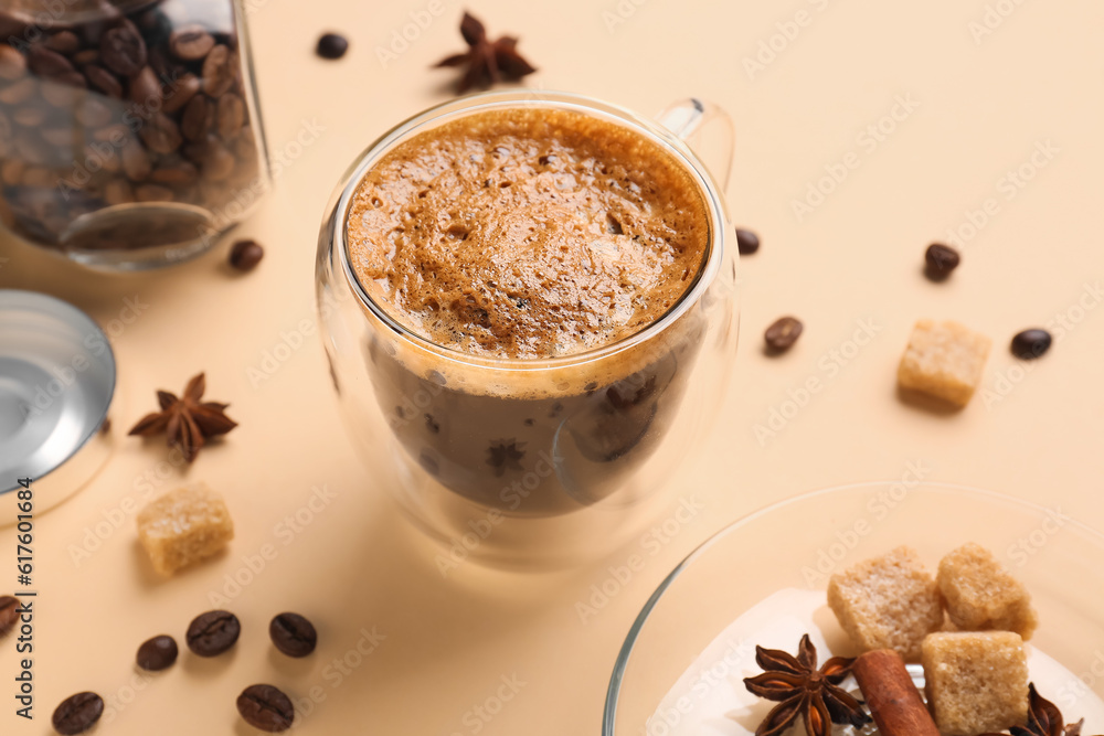 Glass cup of hot espresso and jar with coffee beans on beige background