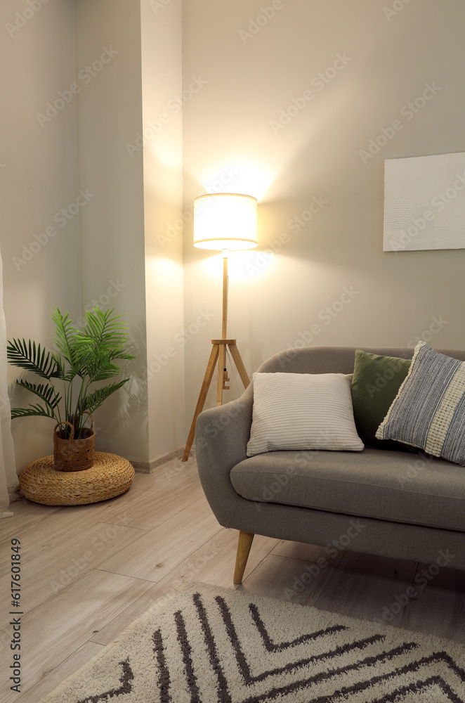 Interior of living room with cozy grey sofa and glowing lamp