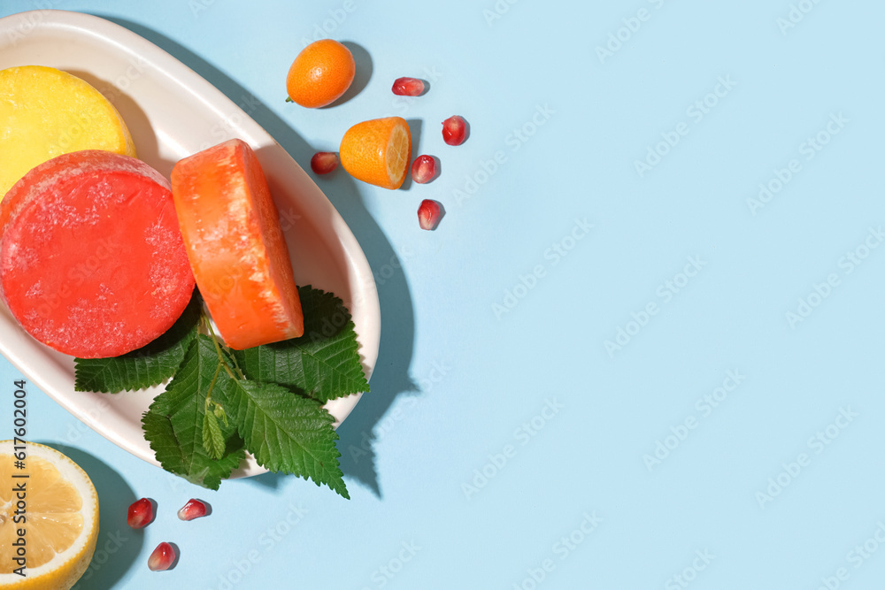 Plate with colorful solid shampoo bars, lemon and leaves on blue background