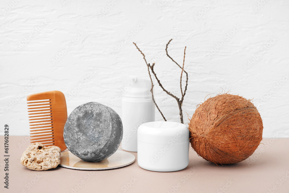 Solid shampoo bar with jars of cosmetic product, comb and coconut on table