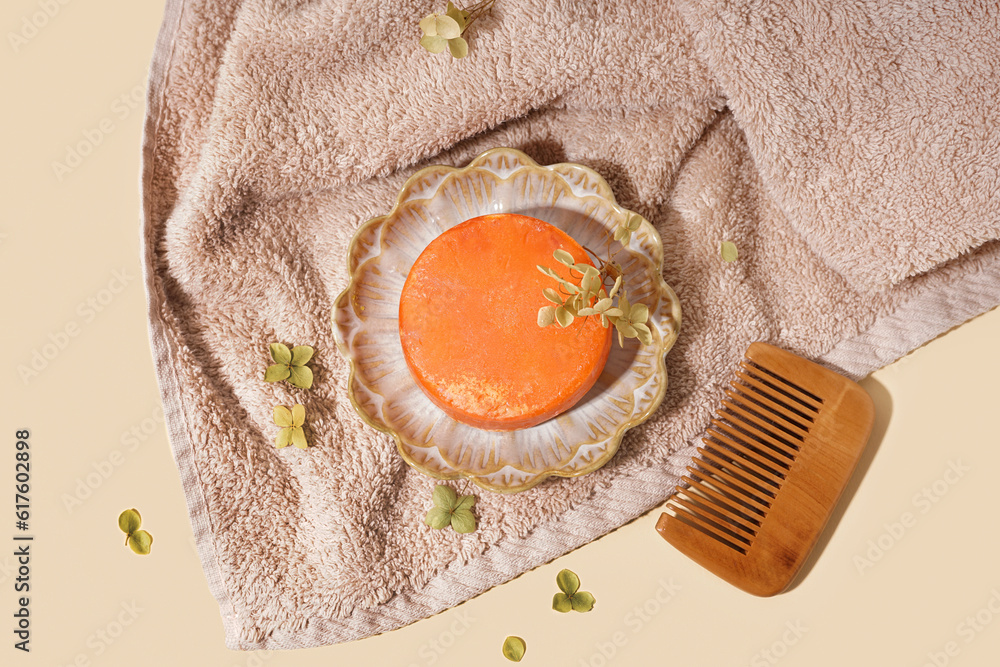 Plate with orange solid shampoo bar, dry lilac and comb on beige background