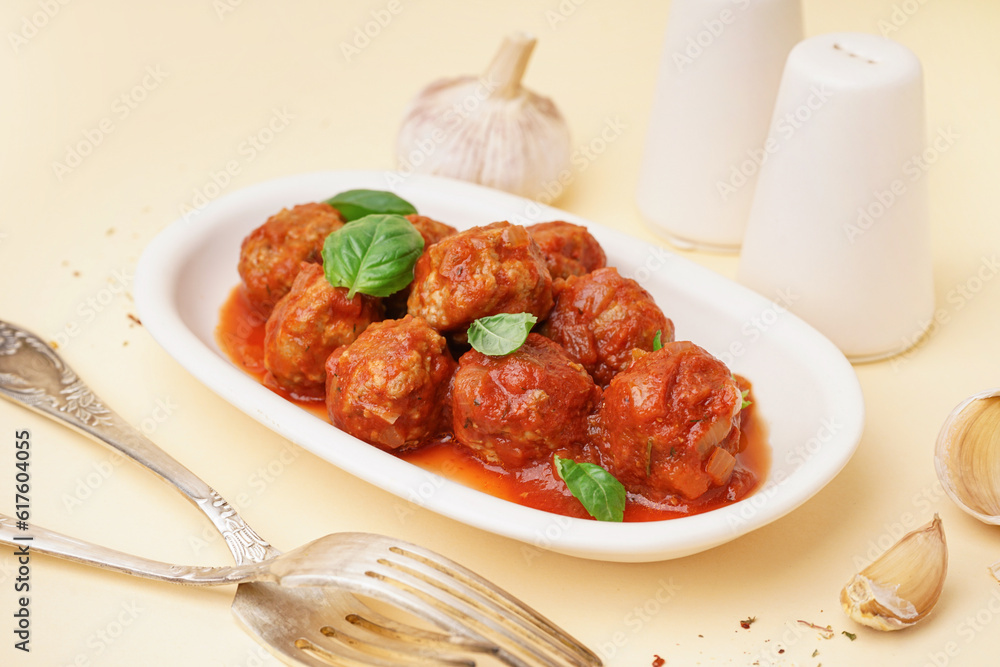 Plate of tasty meat balls with tomato sauce and basil on beige background