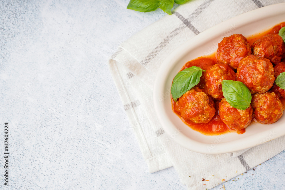 Plate of tasty meat balls with tomato sauce and basil on grey table