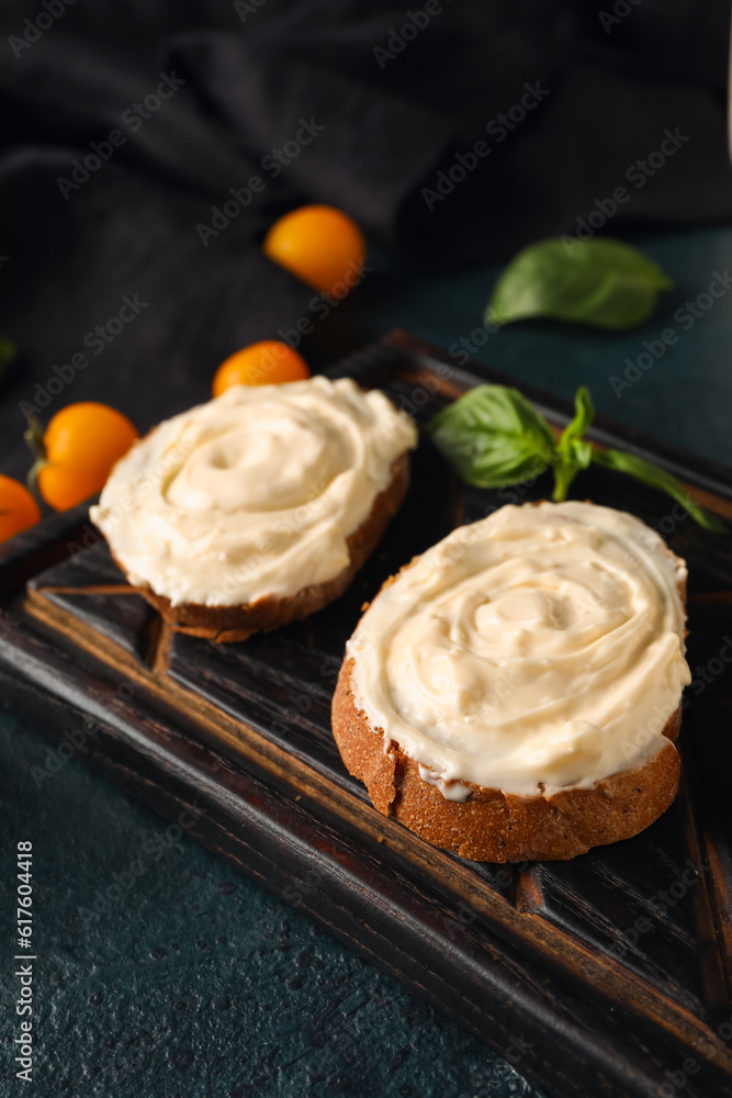 Wooden board of tasty sandwiches with cream cheese on black background