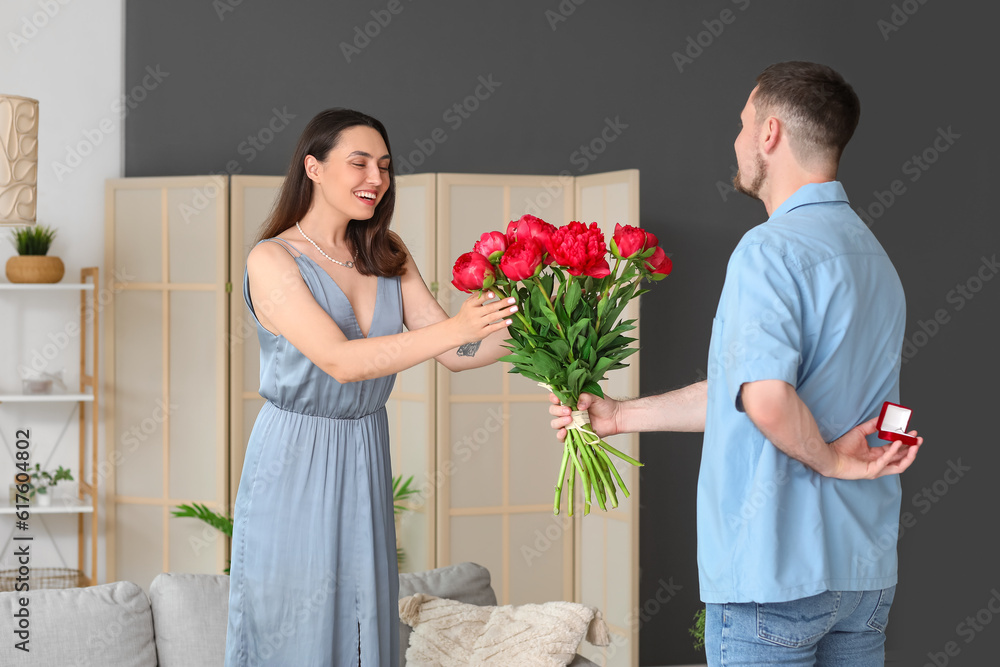 Young man with flowers proposing to his girlfriend at home