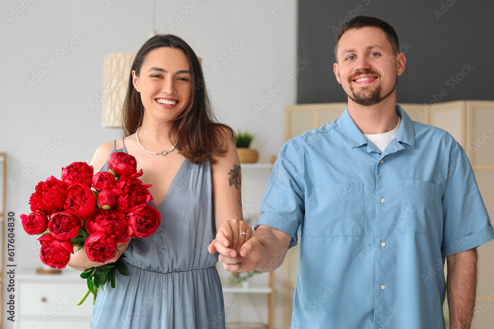 Happy engaged couple with flowers holding hands at home