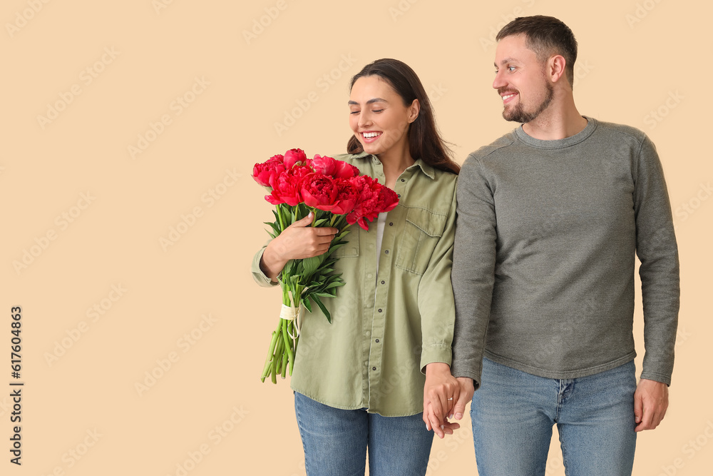 Happy engaged couple with flowers holding hands on beige background