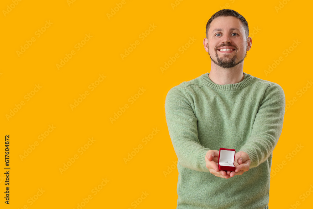 Young man with engagement ring on yellow background