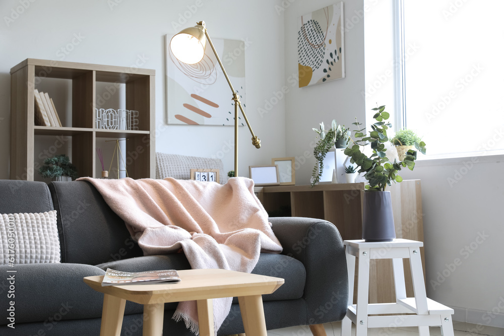 Interior of light living room with glowing lamp, table and sofa