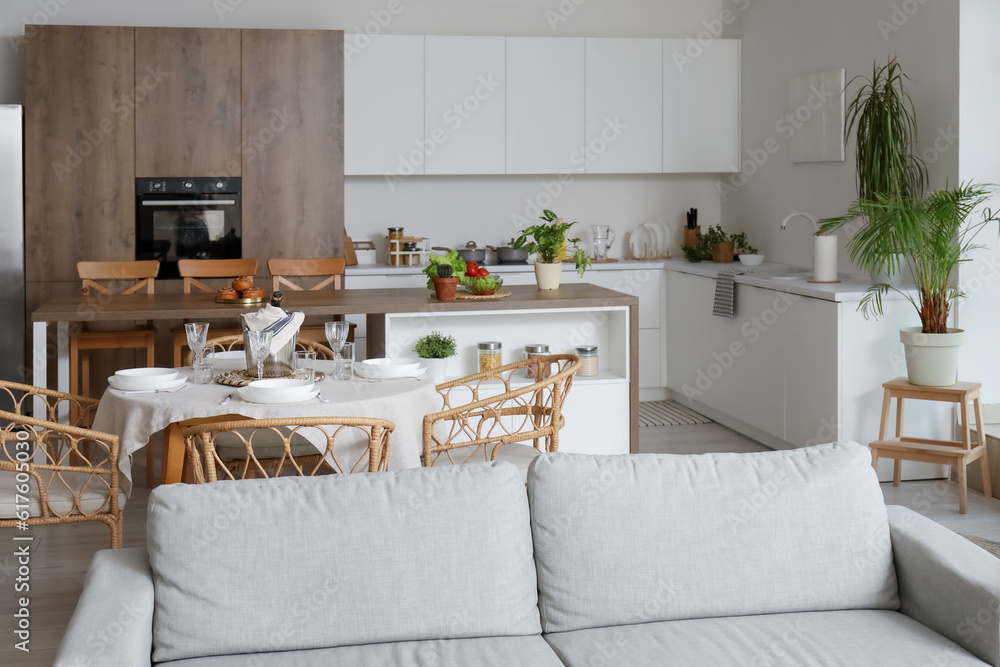 Interior of light open space kitchen with grey sofa, served dining table and island