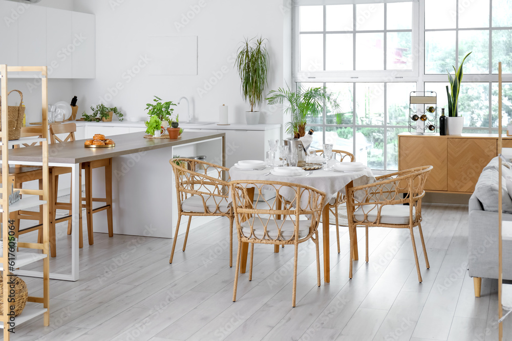 Interior of light open space kitchen with served dining table, island and big window