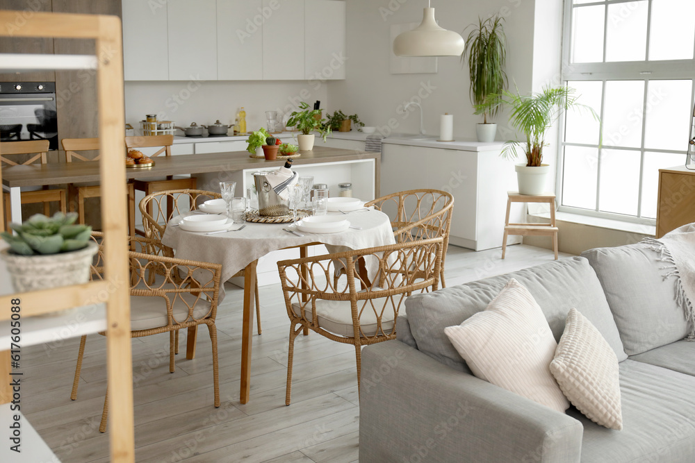 Interior of light open space kitchen with grey sofa, served dining table and island