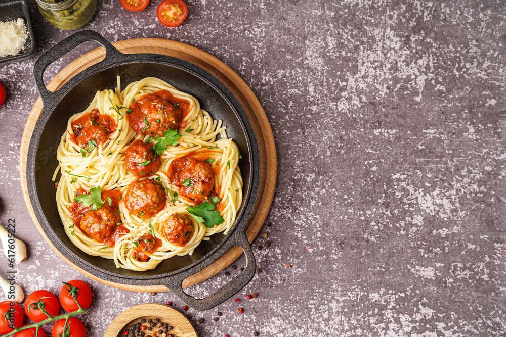 Frying pan of boiled pasta with tomato sauce and meat balls on grey table