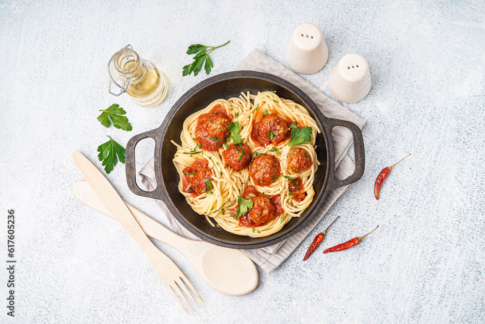 Frying pan of boiled pasta with tomato sauce and meat balls on white table