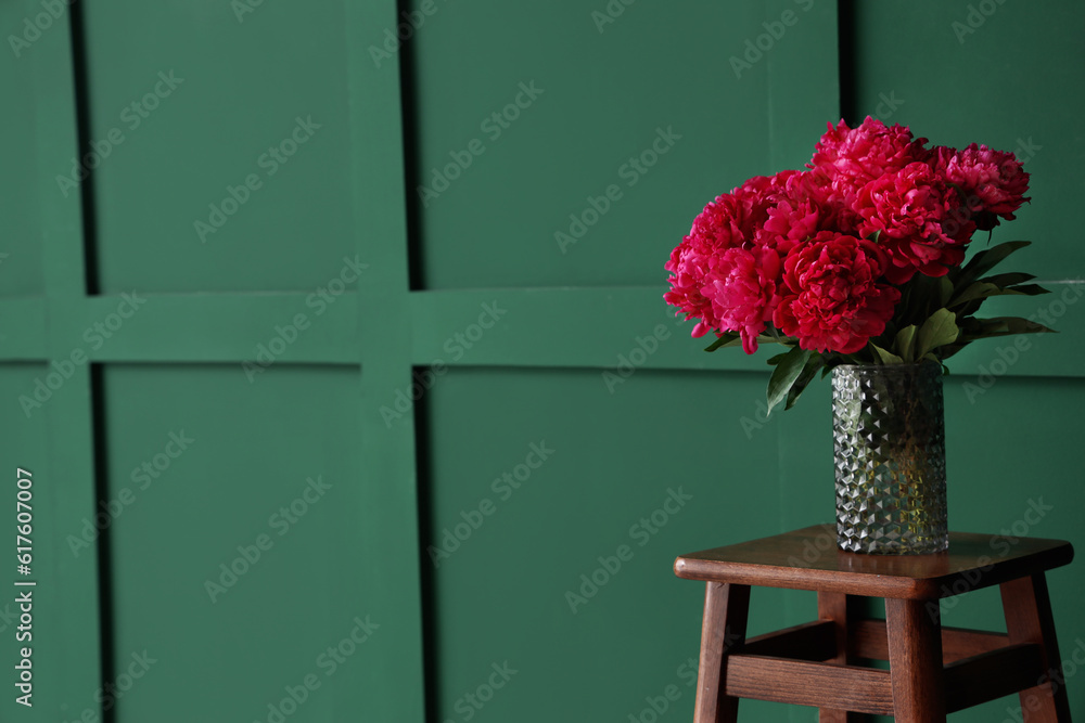 Vase of red peonies on stool near green wall