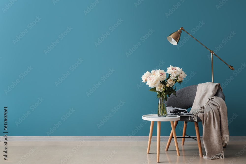 Vase of white peonies with coffee table, chair and floor lamp near blue wall