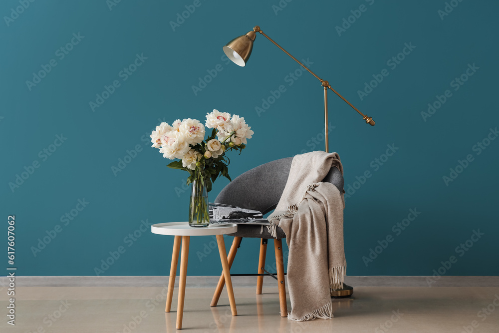 Vase of white peonies with coffee table, chair and floor lamp near blue wall