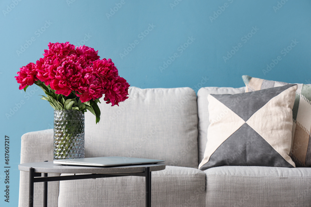 Vase of red peonies with coffee table and couch near blue wall