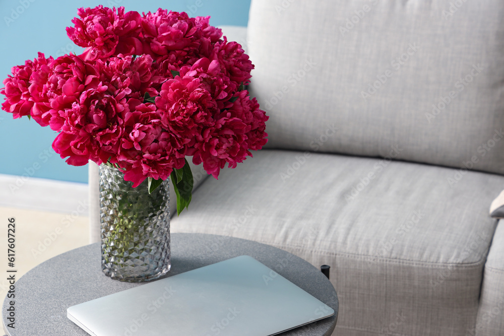 Vase of red peonies with laptop on coffee table near couch